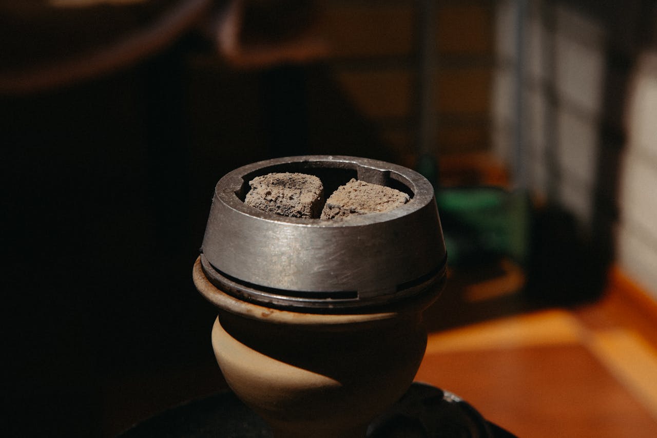 A detailed view of charcoal pieces in a hookah bowl, illuminated by warm indoor lighting.
