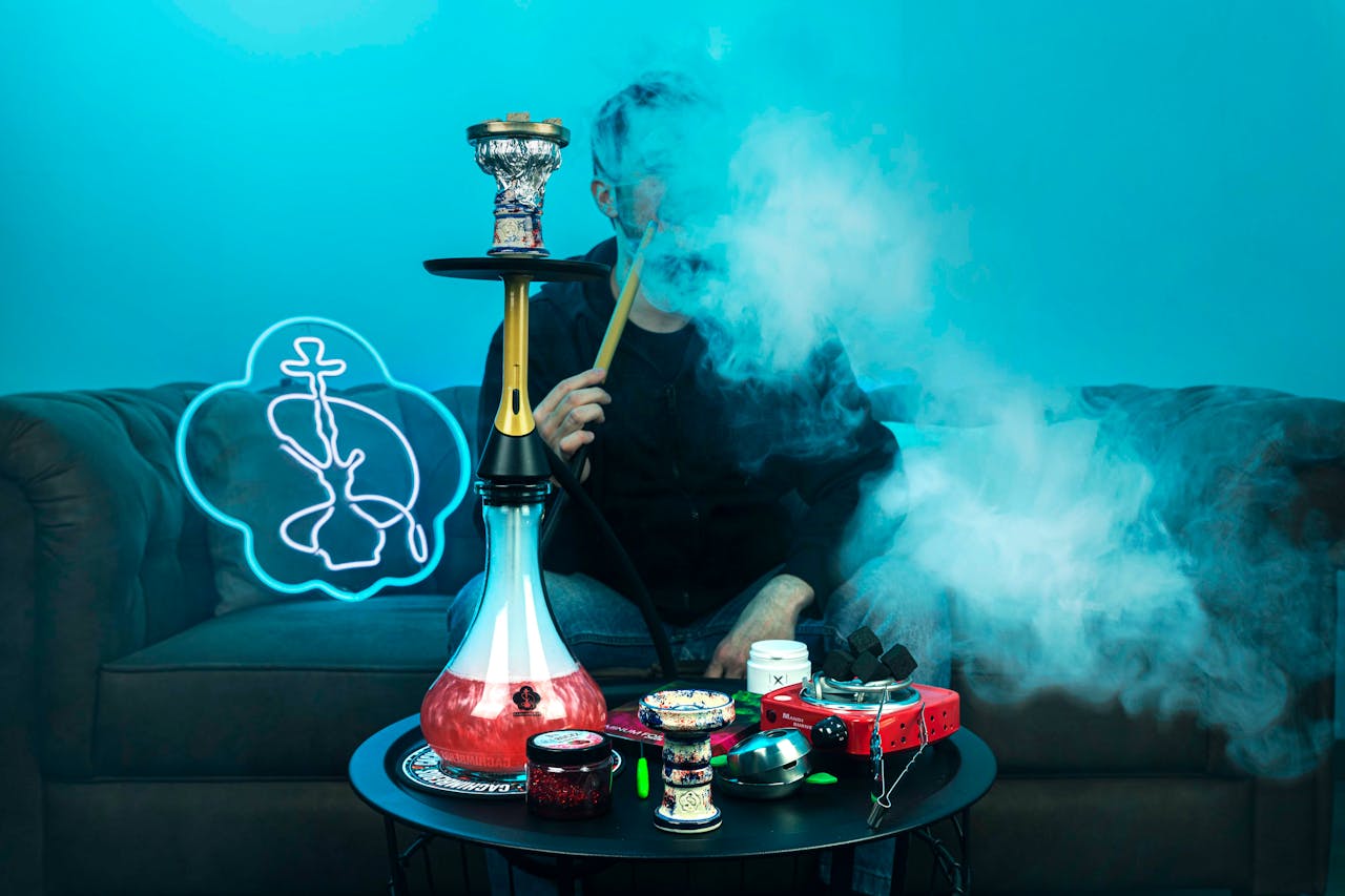 A person smoking hookah indoors with smoke and neon sign creating a relaxed atmosphere.
