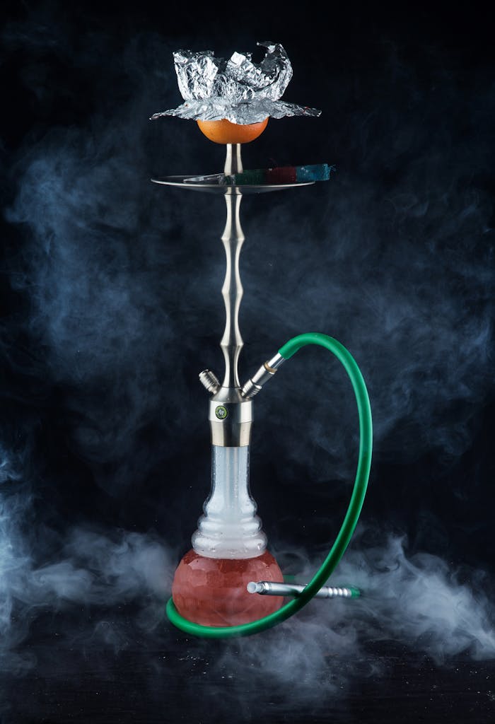 A stylish hookah with a green hose and aromatic smoke rising against a dark background.