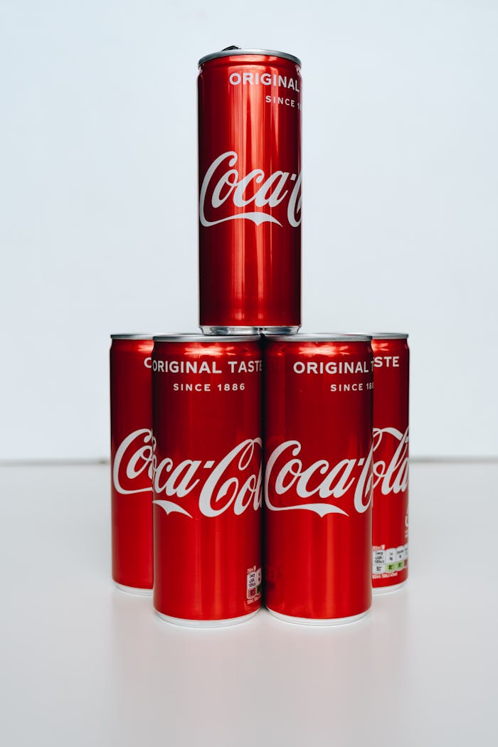 Services Set of Coca-Cola cans arranged in a pyramid on a clean white surface.